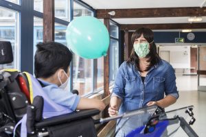 Sozialarbeiterin gibt einem Jungen im Rollstuhl einen Luftballon 