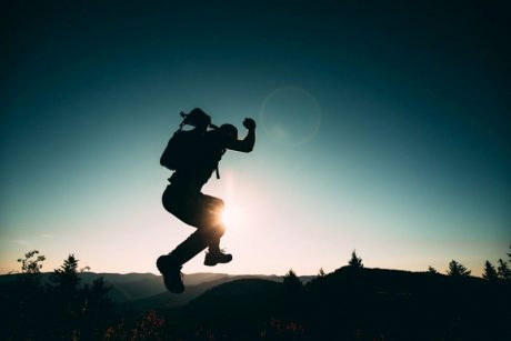 Person mit Rucksack springt in der Dämmerung