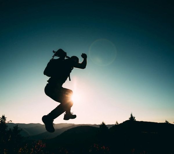 Person mit Rucksack springt in der Dämmerung