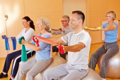 Lächelnde Gruppe macht Reha-Sport mit Gymnastikband im Fitnesscenter