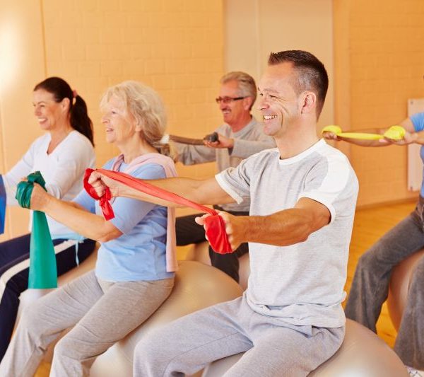 Lächelnde Gruppe macht Reha-Sport mit Gymnastikband im Fitnesscenter