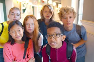 Portrait of multiethnic children looking at camera standing in school building. Diverse curious boys and girls posing at camera standing in corridor having break after classes