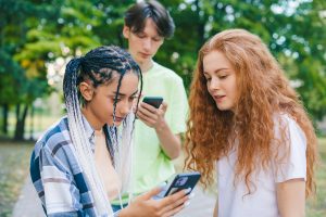 Three caucasian modern teenagers pleased to get many positive reactions on their internet posts. Creating a video for the internet using a smartphone